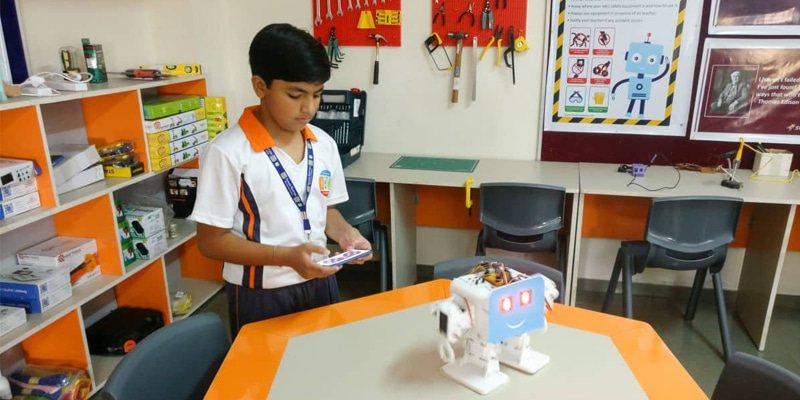 Student using a smartphone to control a small educational robot on a desk.
