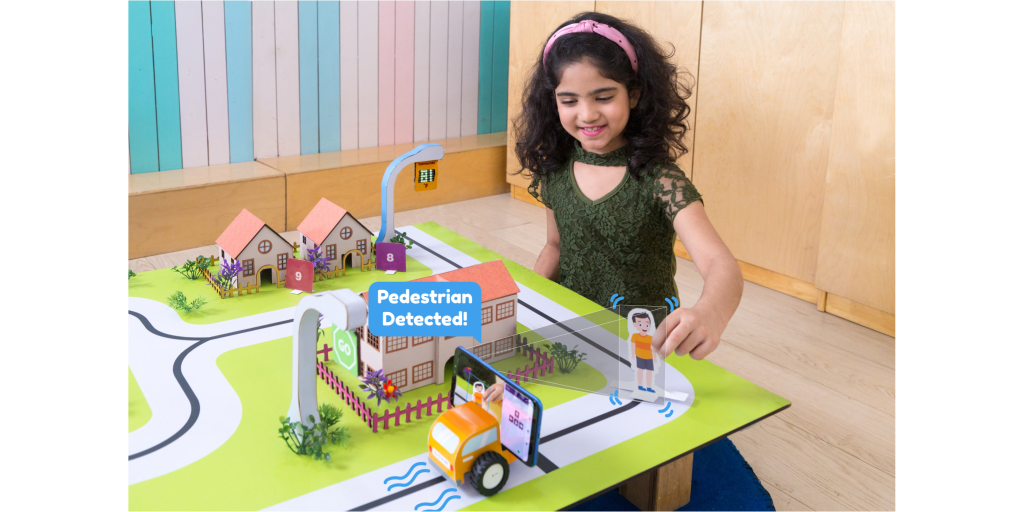 A young girl is playing with a smart city model featuring an interactive car and pedestrian alert system
