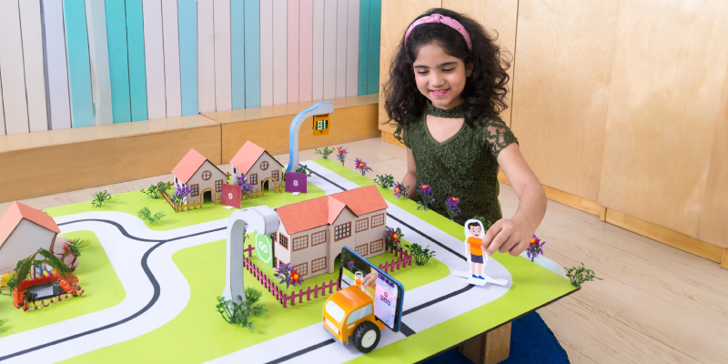 A young girl is playing with a smart city model featuring an interactive car and pedestrian alert system