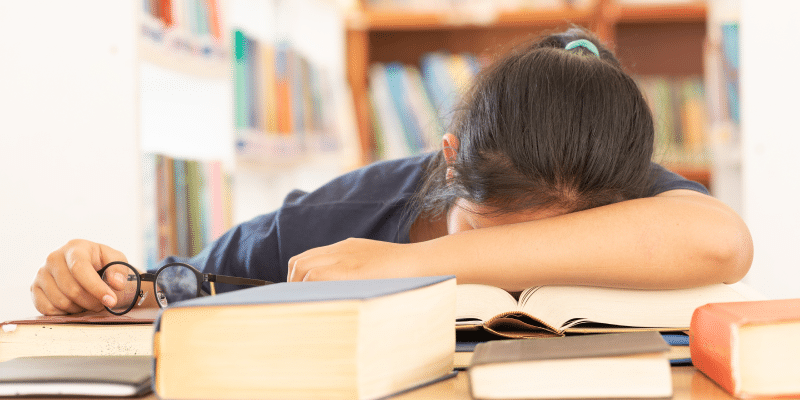 Exhausted student sleeping over books, illustrating the lack of creativity in traditional education