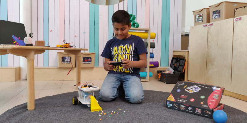 A young boy controlling a DIY vacuum cleaner robot built with the evive Starter Kit, using a smartphone