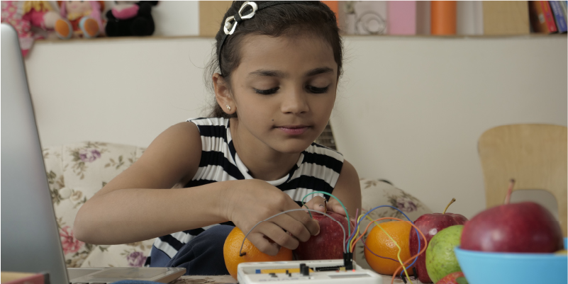 A 7-year-old girl conducting a science experiment with fruits using an evive kit to learn about electric circuits and sensors